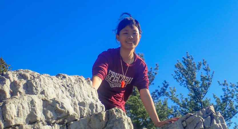 a girl on a rock smiles down at the camera on a backpacking course